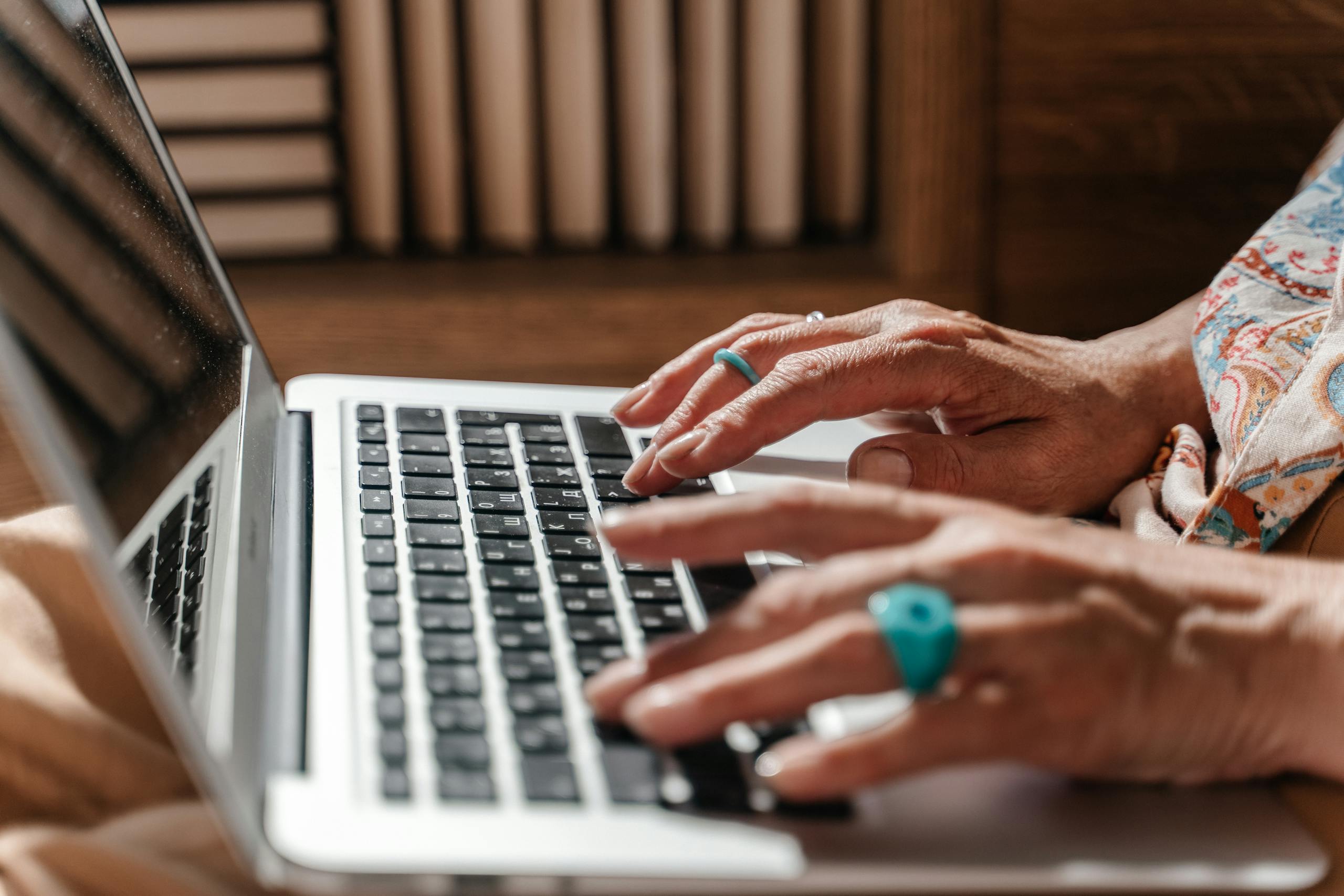 Close-up of an elderly person typing on a laptop in a warm indoor environment, emphasizing digital engagement.