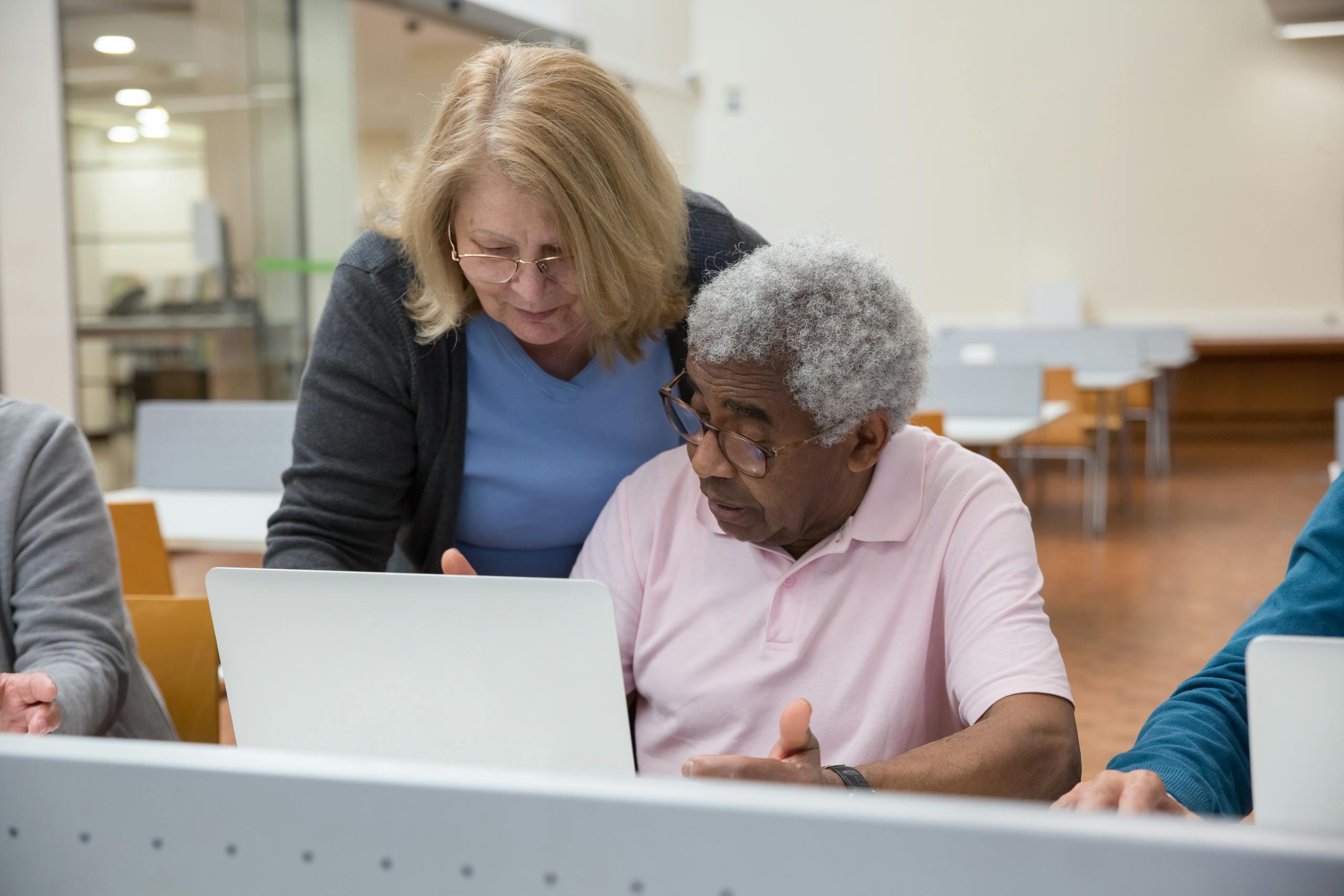 Elderly man and woman in classroom learning to use laptops, showcasing senior education and technology skills.